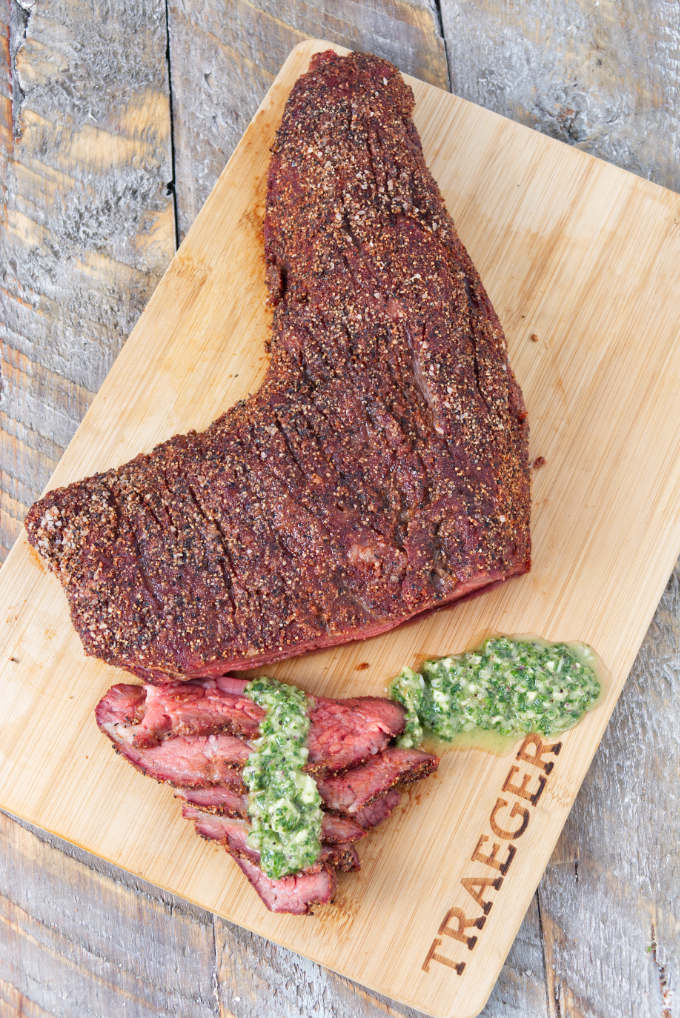 Traeger smoked tri-tip sliced on a cutting board topped with chimichurri