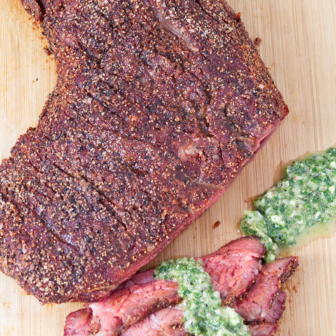 Traeger smoked tri-tip sliced on a cutting board topped with chimichurri