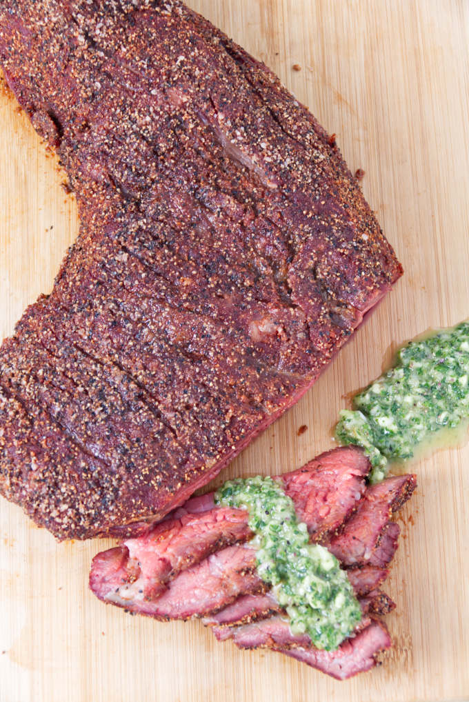 Traeger smoked tri-tip sliced on a cutting board topped with chimichurri