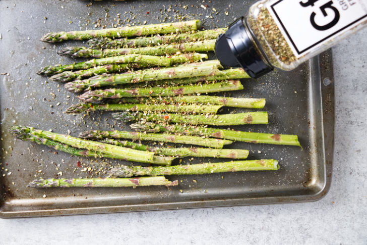 Adding seasoning to asparagus.