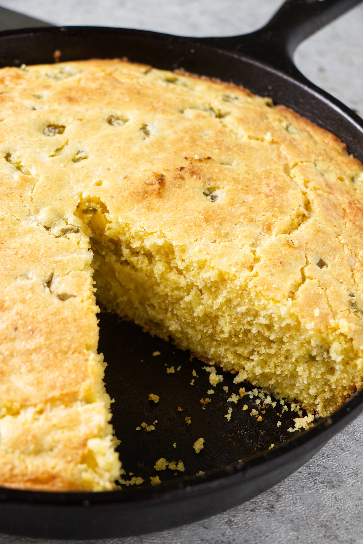 Cornbread in a cast iron skillet with a slice removed.