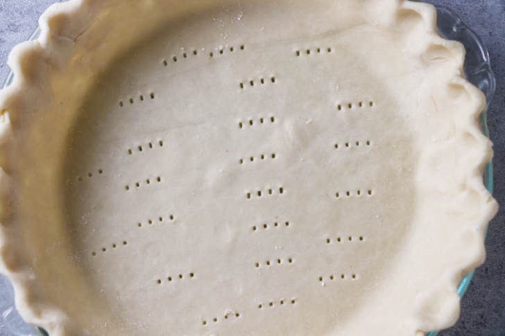 Poking holes in the bottom of a pie crust before baking it.
