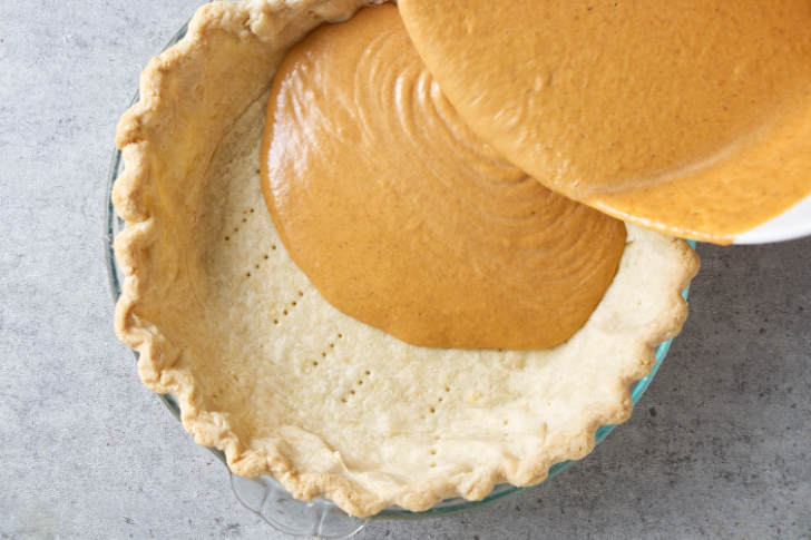 Pouring pumpkin pie filling into a pie shell.