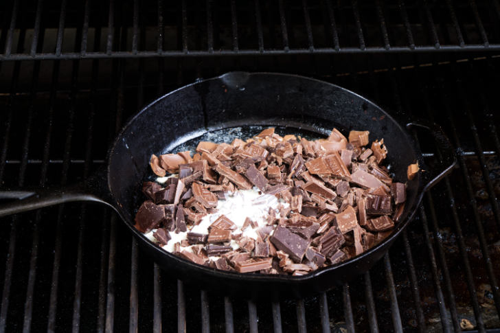 Melting chocolate and cream in a skillet on a grill.