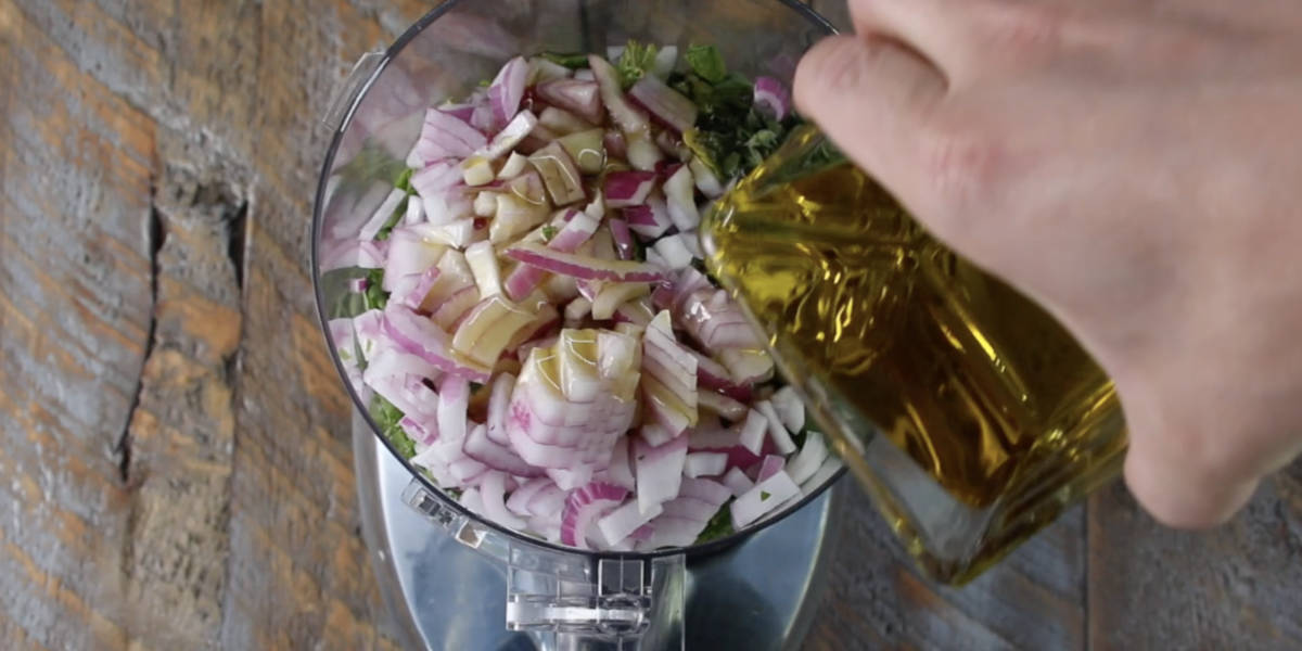 pouring olive oil into the food processor after adding the rest of the chimichurri ingredients