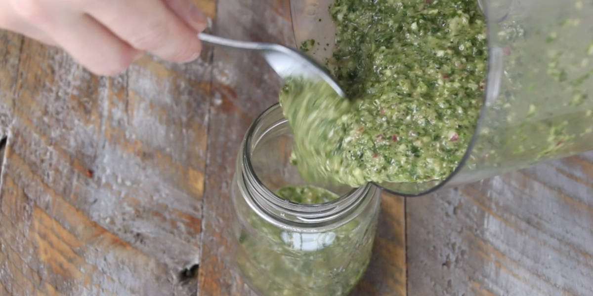 dumping chimichurri into mason jar from food processor