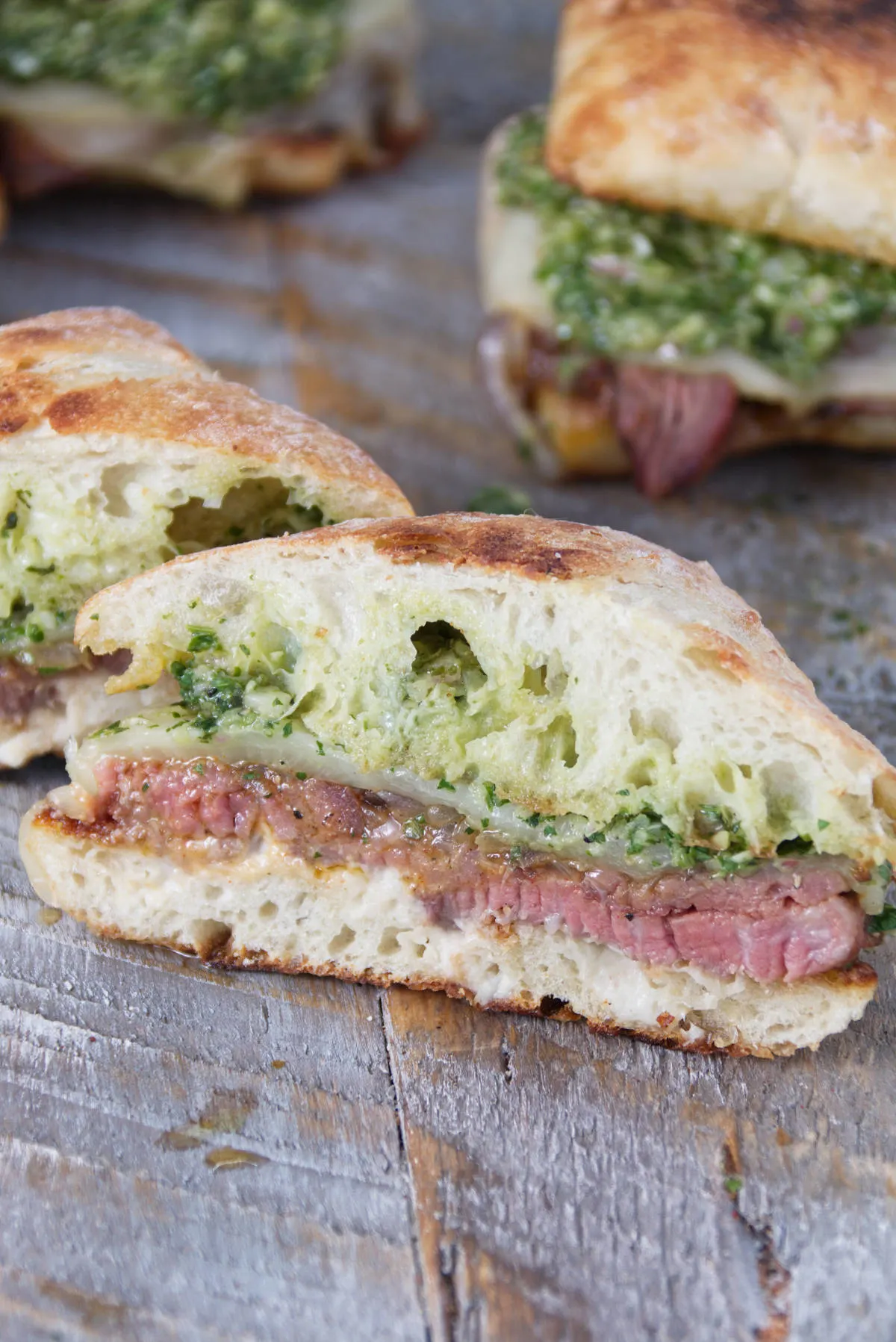 tri-tip sandwiches on a ciabatta roll with herby minto cilantro chimichurri and melted provolone cheese sliced in half diagonally