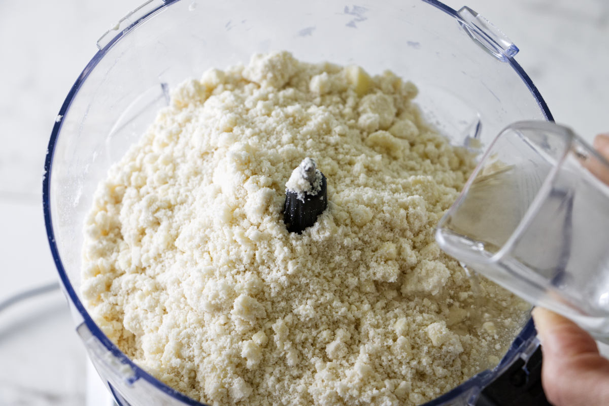 Adding liquid to pie crust ingredients in a food processor.