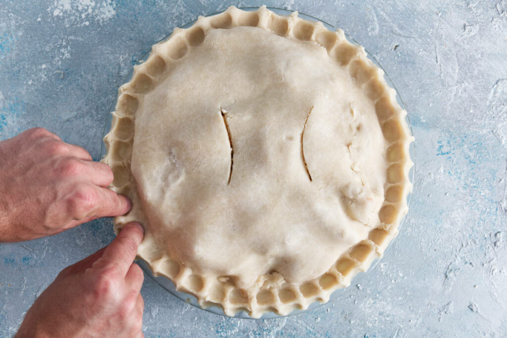 pinching the edges of the pie crust to seal in the apple pie filling