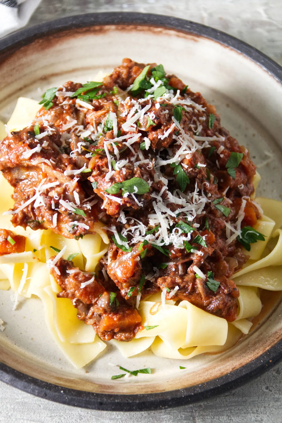 short rib ragu sauce served over pappardelle pasta on a plate and finished with grated parmesan and parsley.