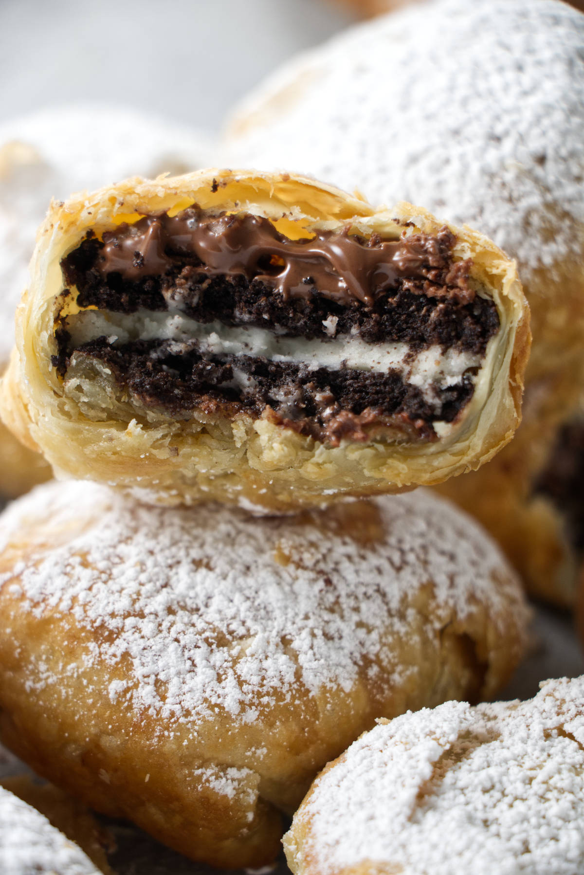 stack of air fried oreos with one in the middle that has been bitten into with nutella oozing out and a crumbly puff pastry shell.
