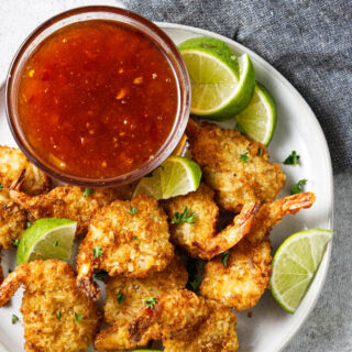 A plate of coconut shrimp and lime wedges next to a dish of dipping sauce.