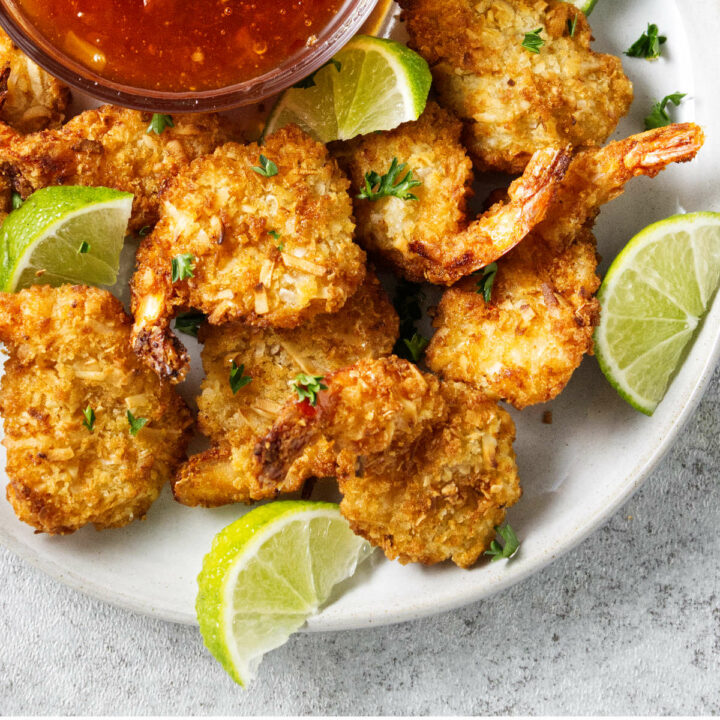 Coconut shrimp on a plate with lime wedges and chili dipping sauce.