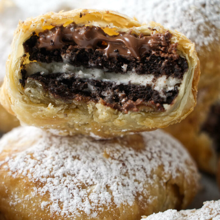 stack of air fried oreos with one in the middle that has been bitten into with nutella oozing out and a crumbly puff pastry shell.