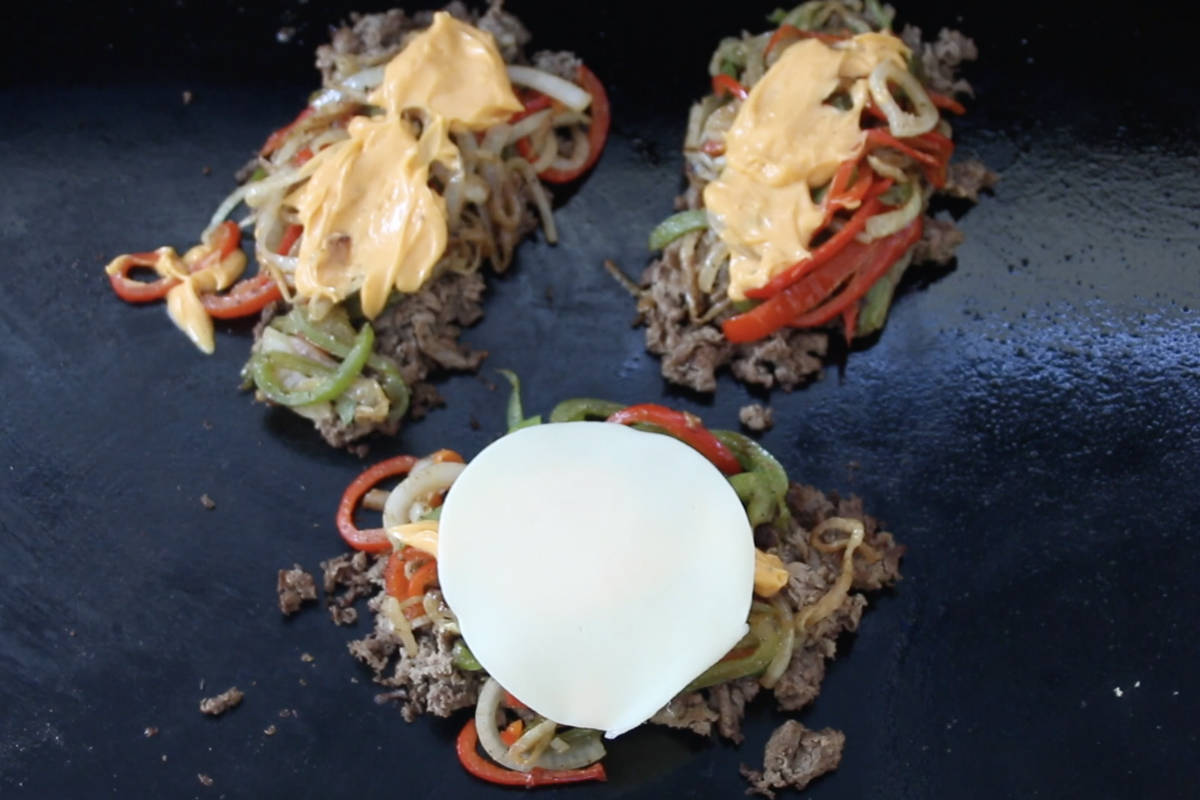 piles of cooked sliced steak with sautéd onions and peppers and topped with melted cheese