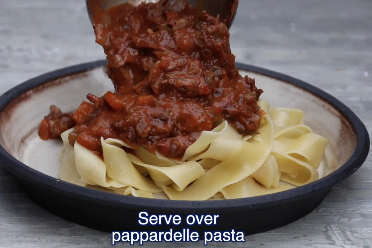 pouring ragu over pappardelle pasta on plate