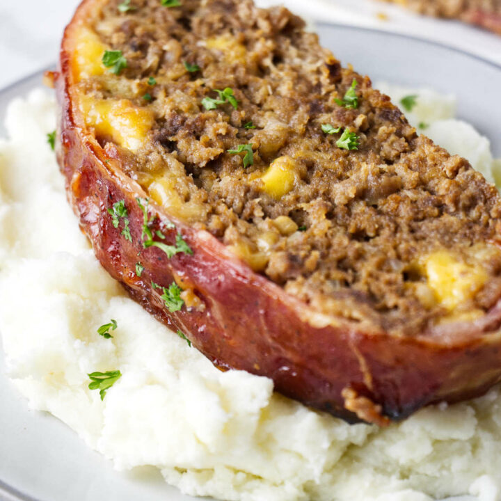Slice of bacon wrapped meatloaf on a bed of mashed potatoes.