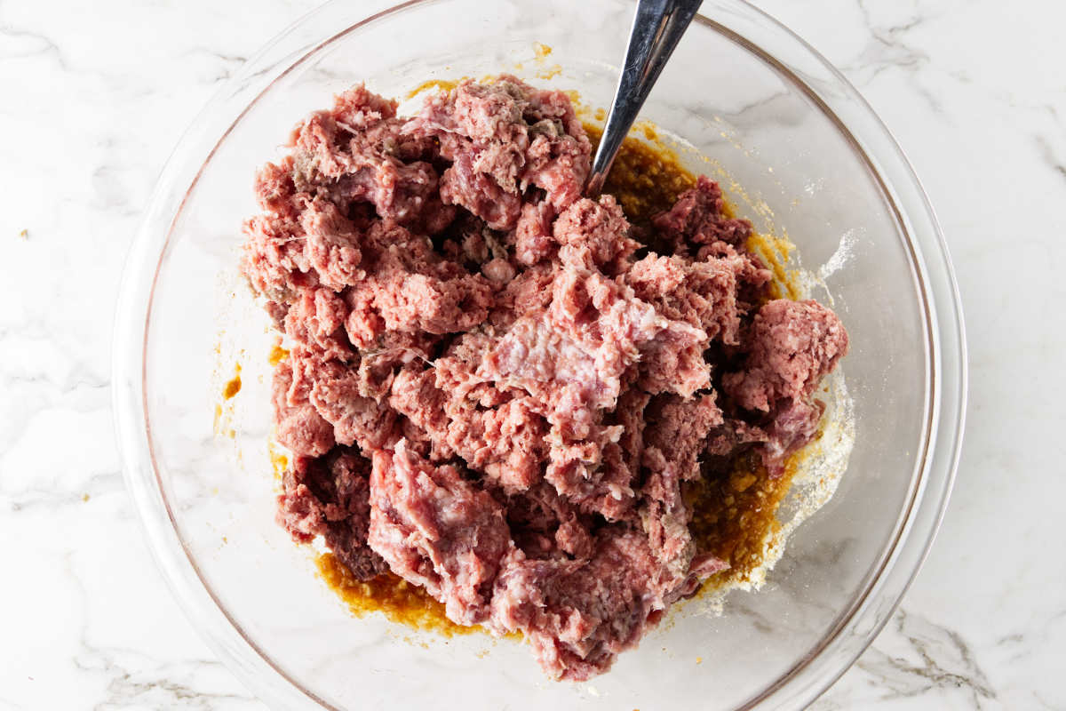 Combining ground beef and pork sausage in mixing bowl.