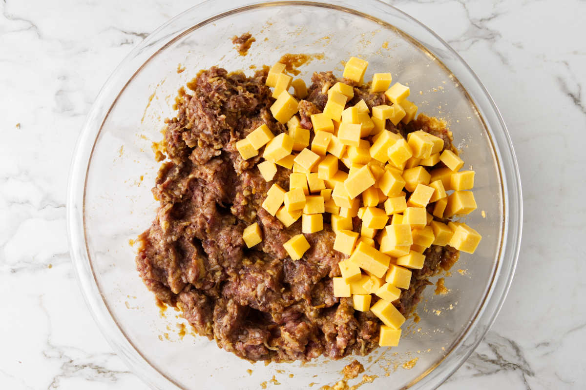 Tossing in cubed cheddar cheese to meatloaf mixture in mixing bowl.