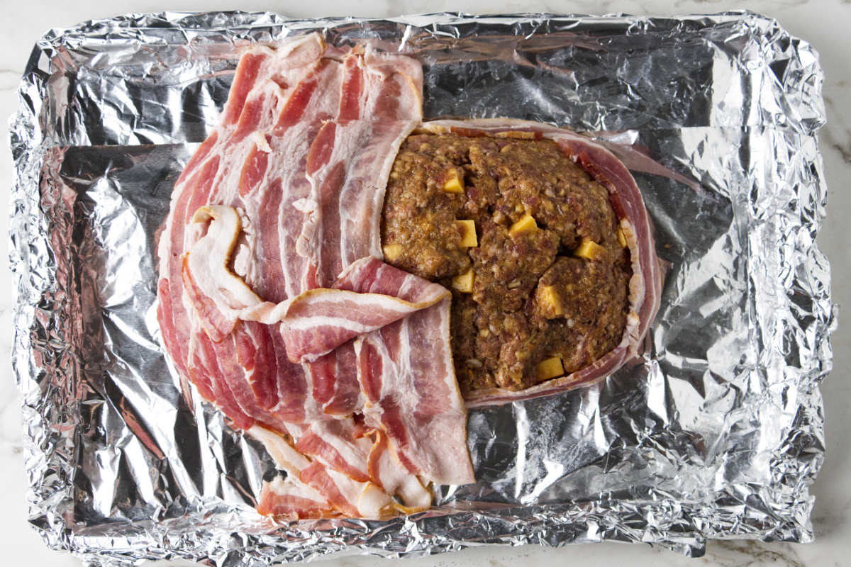 Topping meatloaf with thinly-sliced bacon.