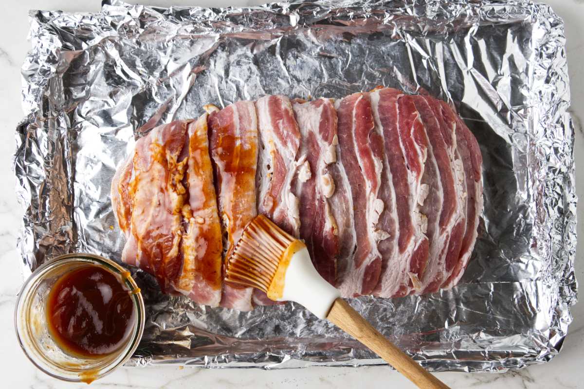 Brushing BBQ sauce on top of the bacon wrapped meatloaf.