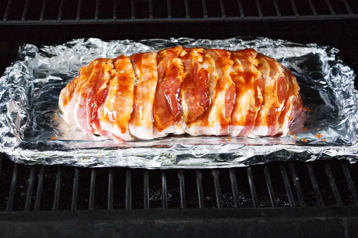 Placing the Traeger smoked bacon wrapped meatloaf on the pellet grill.