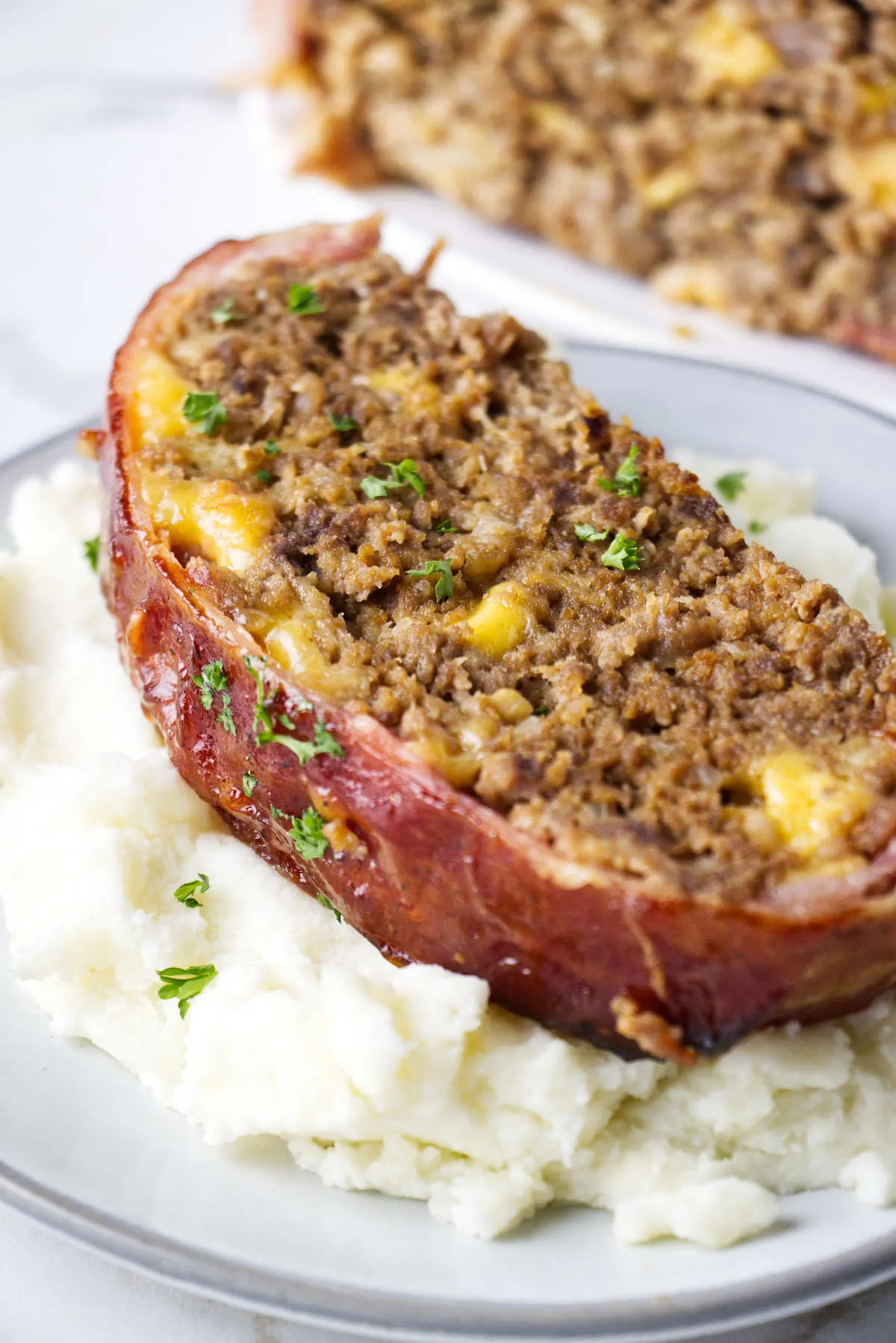 Close up of the smoked bacon wrapped meatloaf sitting on a bed of mashed potatoes. 