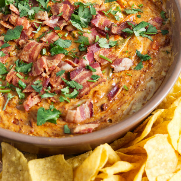 large bowl of queso dip topped with bacon and cilantro with chips