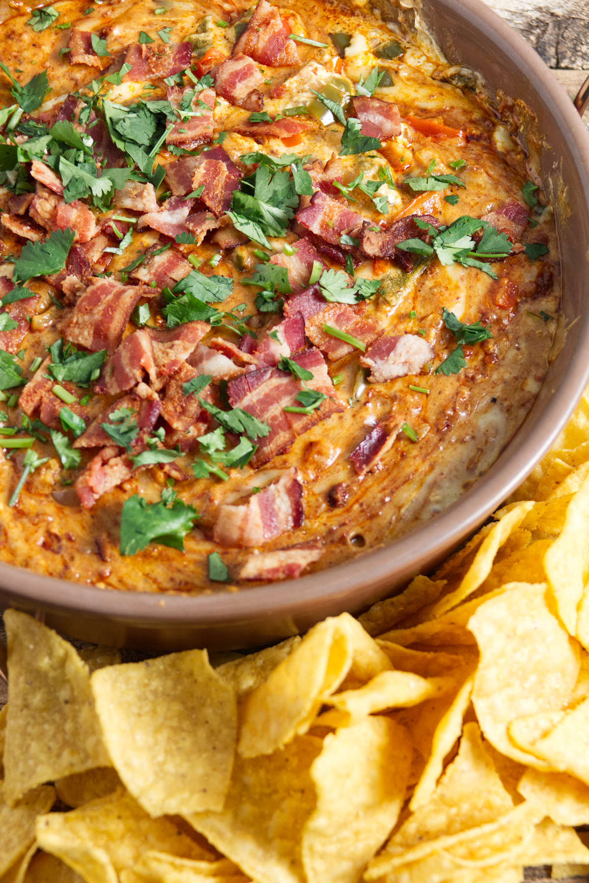 large bowl of queso dip topped with bacon and cilantro with chips