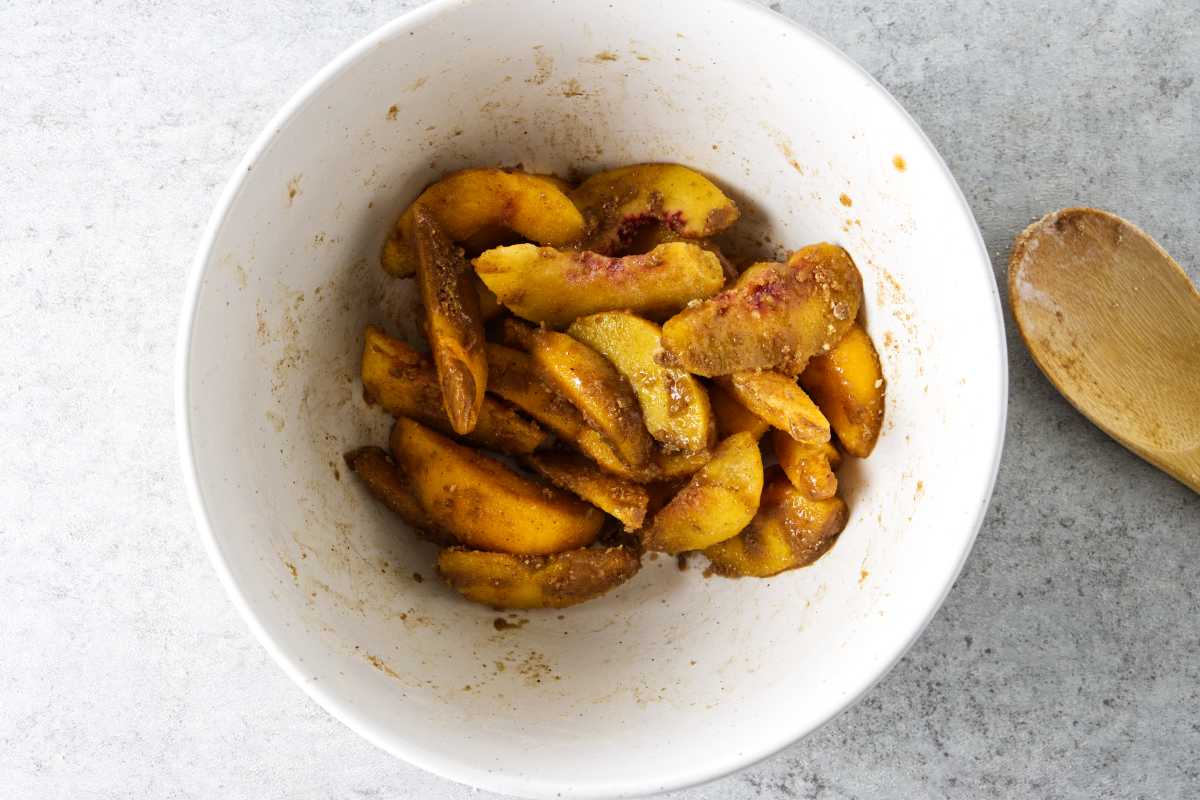 mixing bowl of frozen peaches with seasoning and sugar