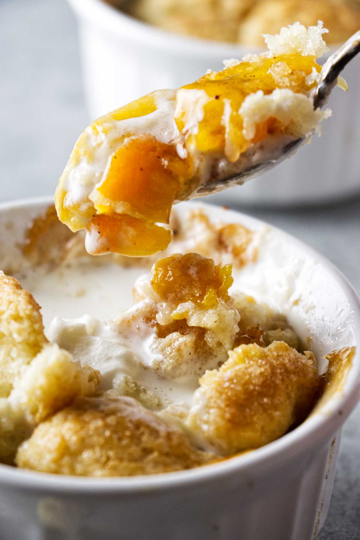 fork with peach hovering over a ramekin filled with peach cobbler