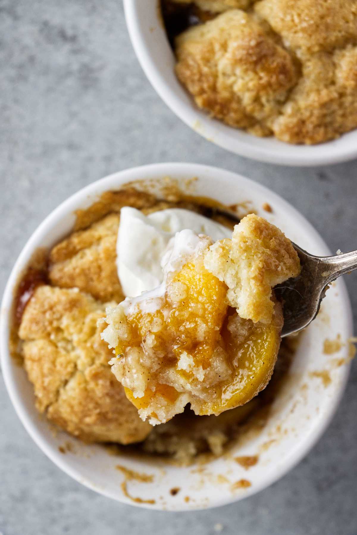 a fork full of peach cobbler hoving over a ramekin filled with the dessert