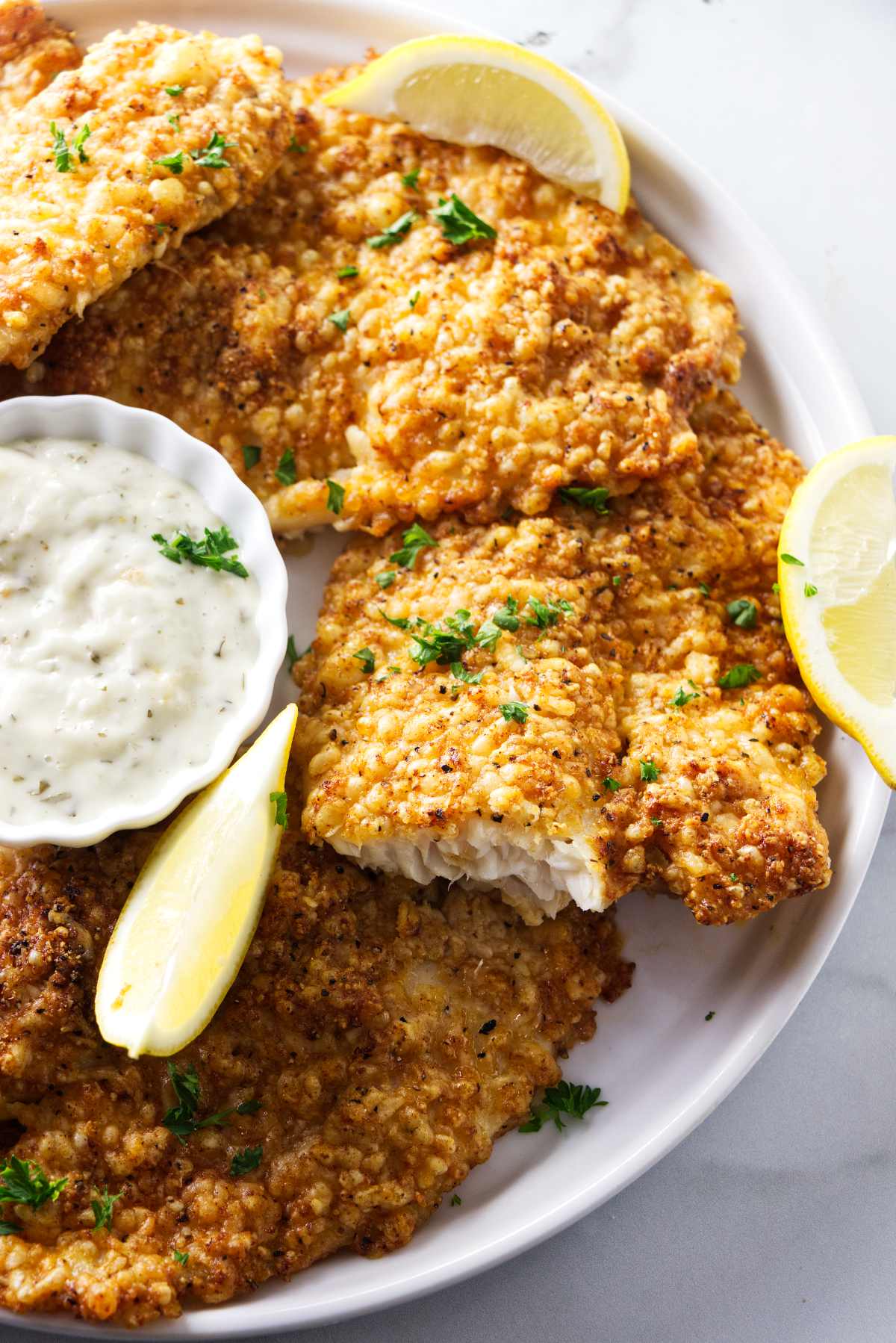 Several air fried tilapia filets on a plate with tartar sauce.