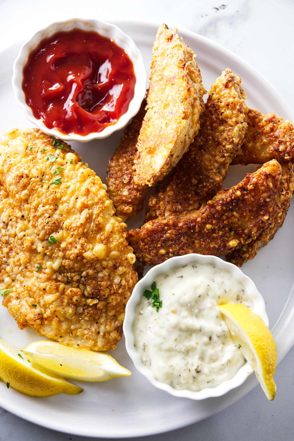 Tilapia and air fried potatoes on a plate with lemon wedges and tartar sauce.