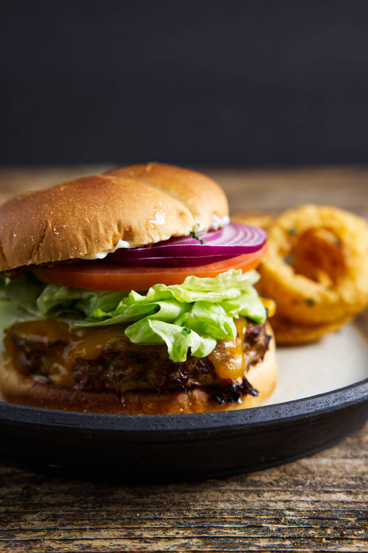 Turkey burger on a brioche bun and loaded with toppings, plated with onion rings.