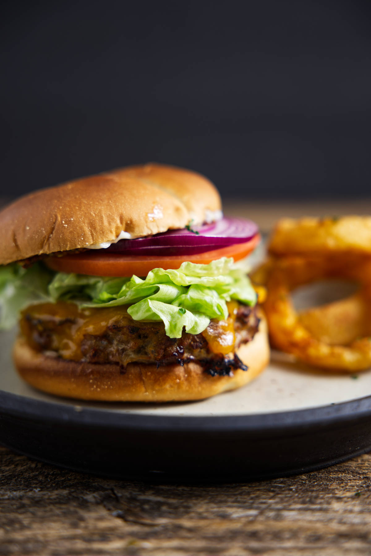 Turkey burger on a brioche bun and loaded with toppings, plated with onion rings.