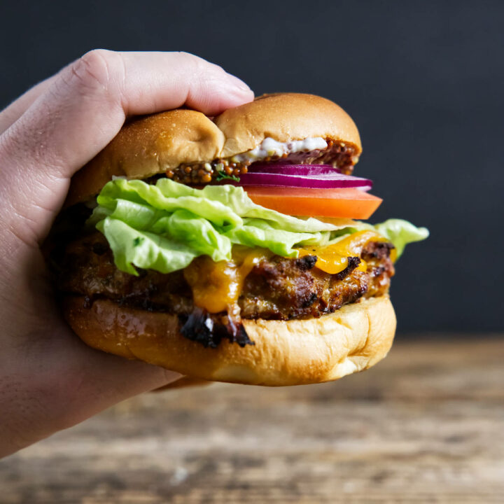 Fully assembled turkey burger being held by hand with cheese oozing.