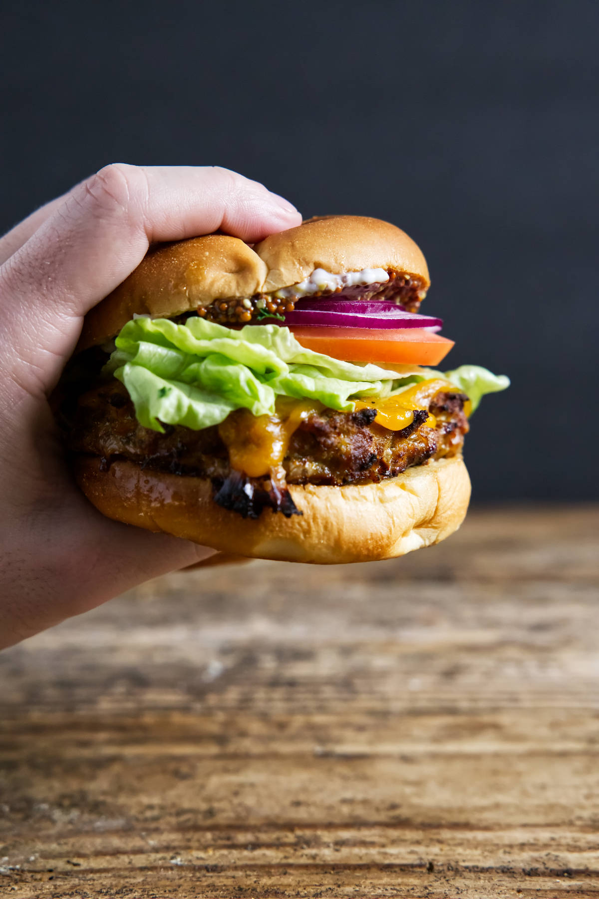 Fully assembled turkey burger being held by hand with cheese oozing.