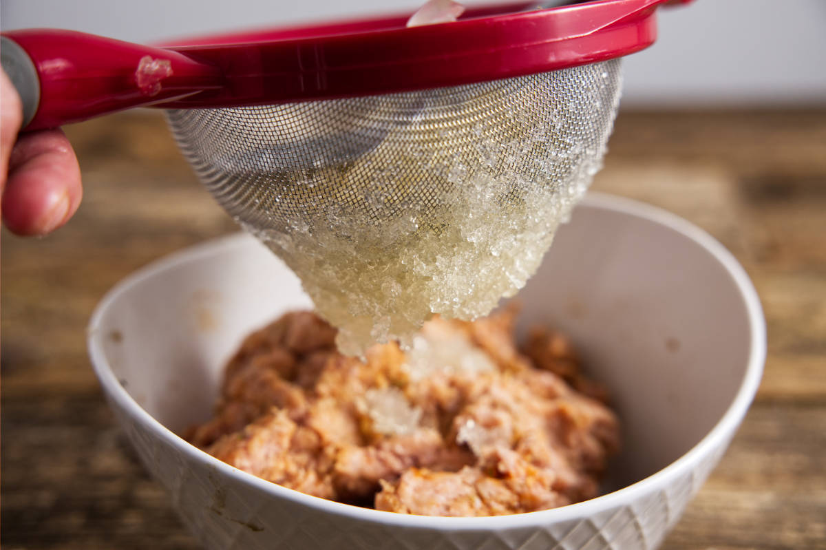 Pushing chicken stock gellatin through a mesh strainer.