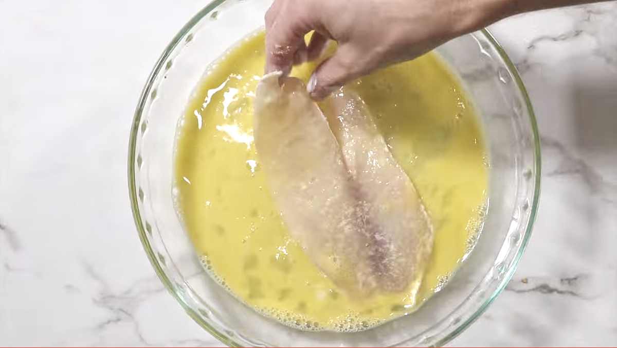 Dipping a tilapia fish filet in egg wash.