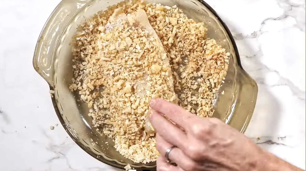 Dipping a fish filet in parmesan coating.