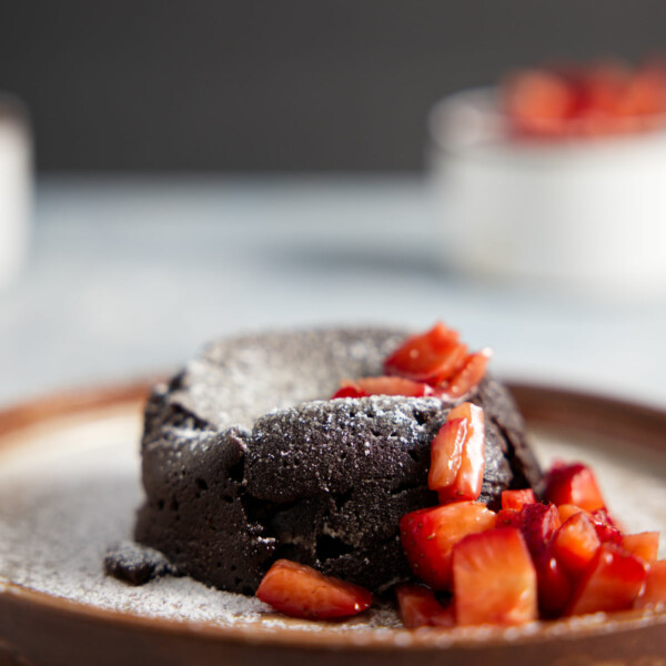 Air fryer mug cake plated with chopped strawberries and dusted with powdered sugar.