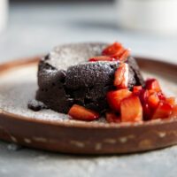 Air fryer mug cake plated with chopped strawberries and dusted with powdered sugar.