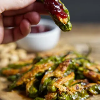 air fryer stuffed shishito peppers, one held in fingertips with a red cherry preserves topping