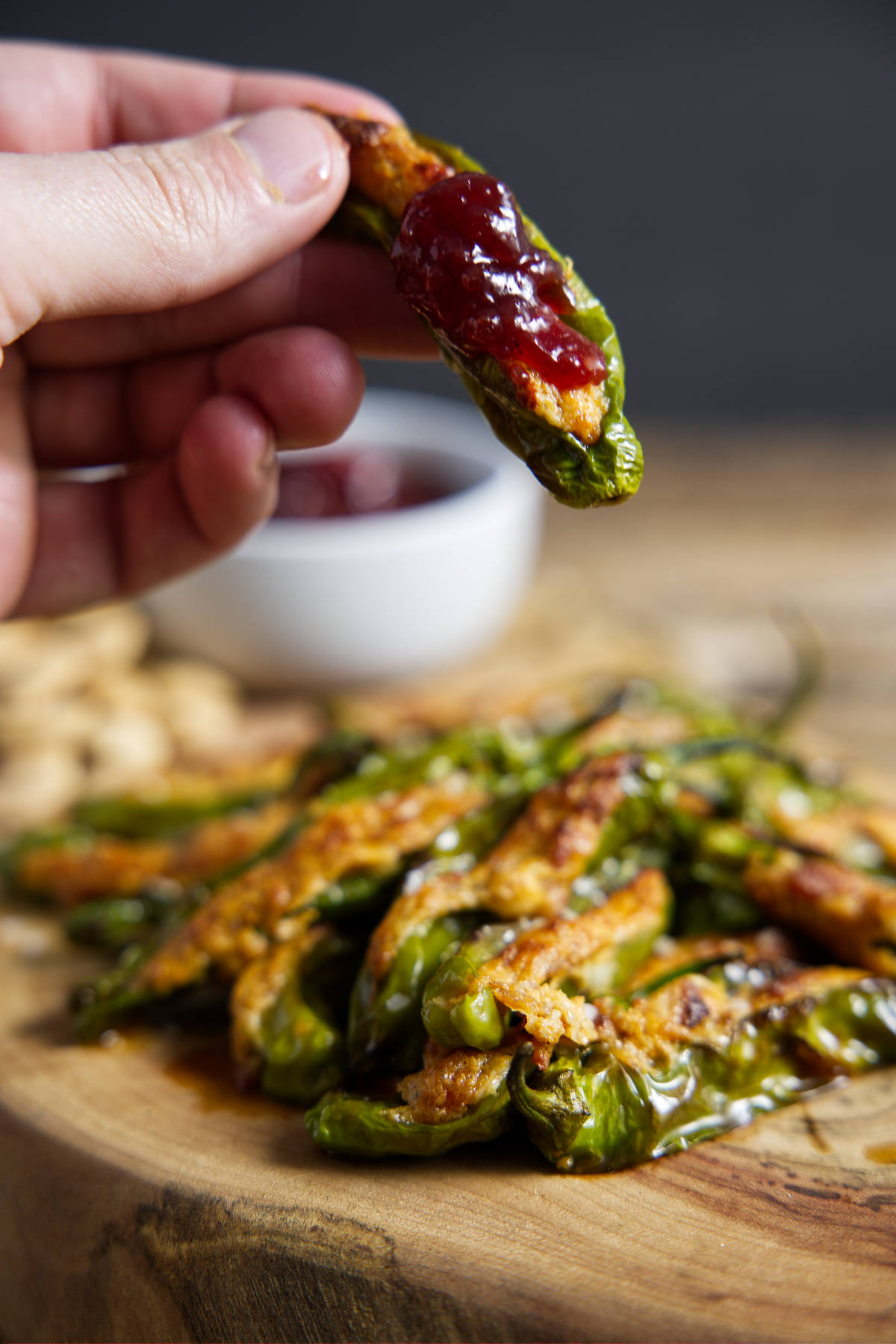 air fryer stuffed shishito peppers, one held in fingertips with a red cherry preserves topping