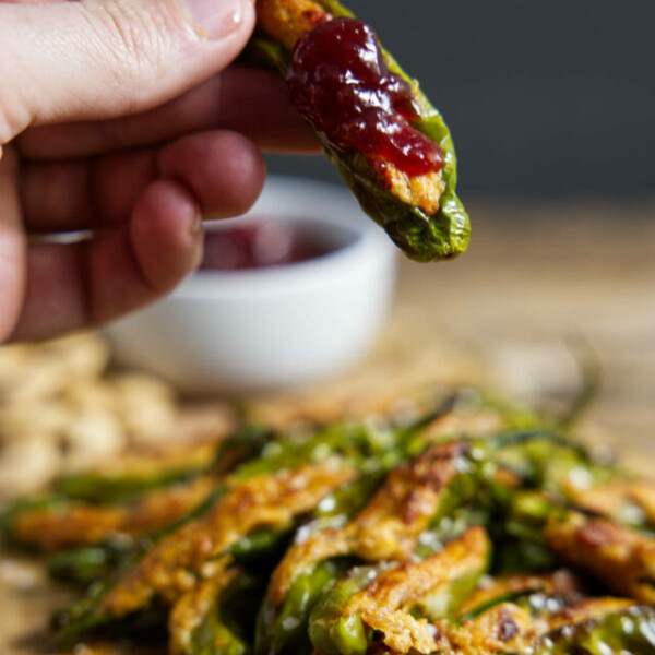 air fryer stuffed shishito peppers, one held in fingertips with a red cherry preserves topping