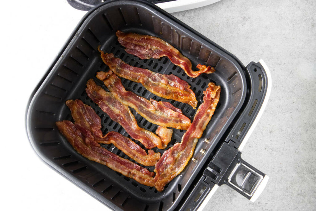 Cooked bacon in an air fryer basket.