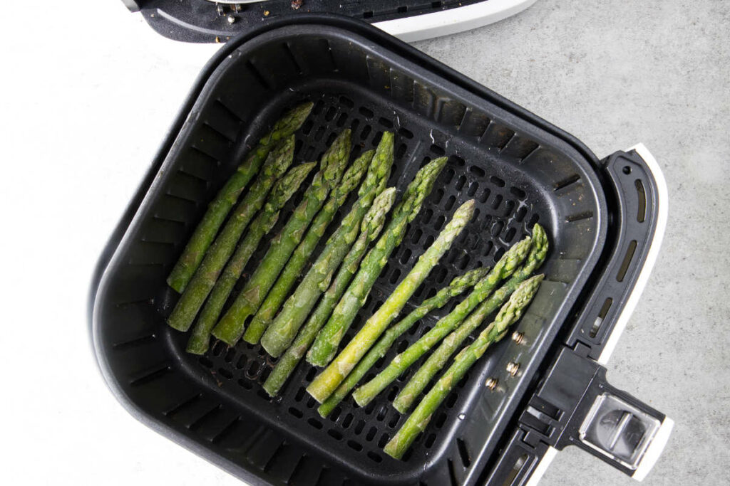 Frozen asparagus in air fryer basket.
