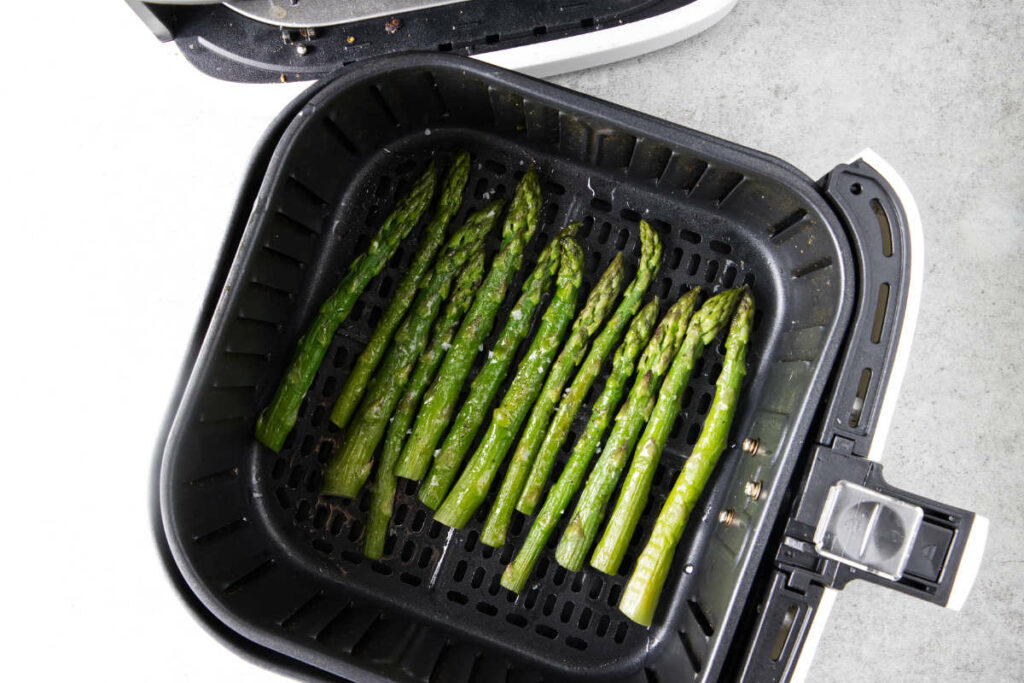 Cooked asparagus in air fryer basket.