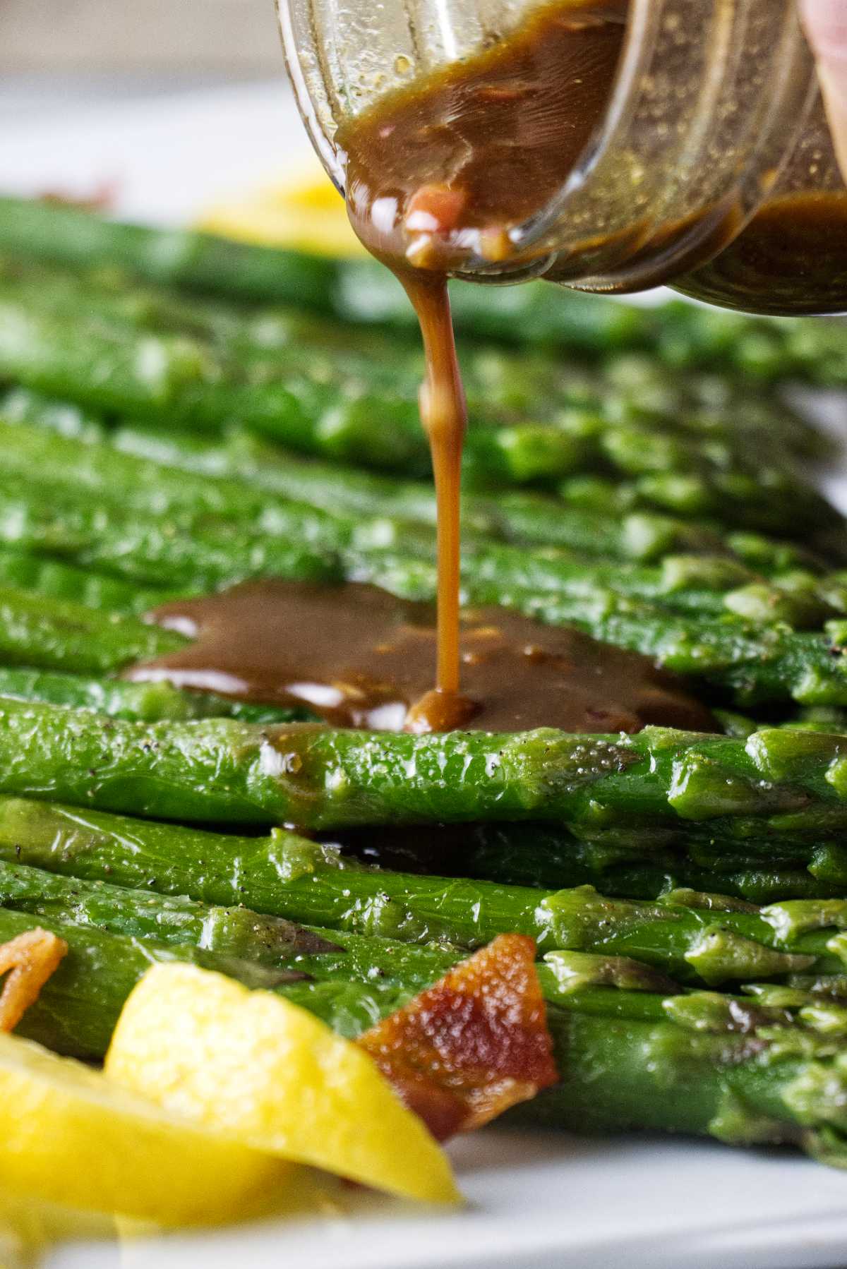 Drizzling vinaigrette over cooked asparagus on a plate.